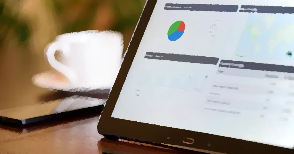 Close-up of a tablet displaying analytics charts on a wooden office desk, alongside a smartphone and coffee cup.