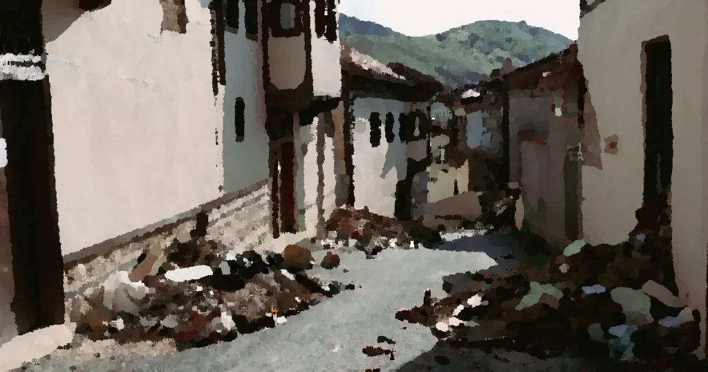 Devastation from an earthquake shown on a narrow village street in Malatya, Turkey, with debris and ruined buildings.