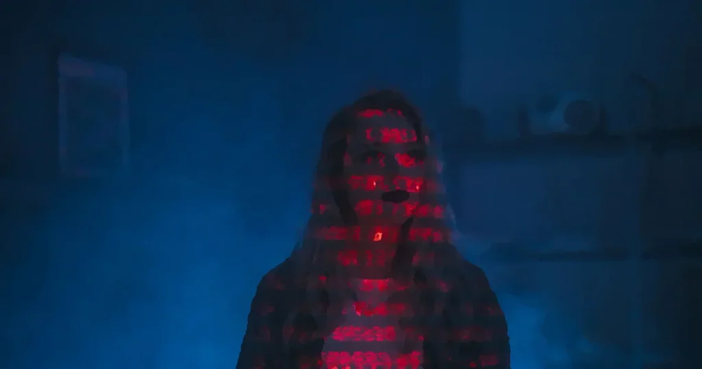A mysterious silhouette with red binary code projected over the face, set against a dark, moody background.