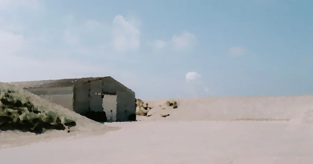 A solitary hangar surrounded by sandy dunes under a bright blue sky.