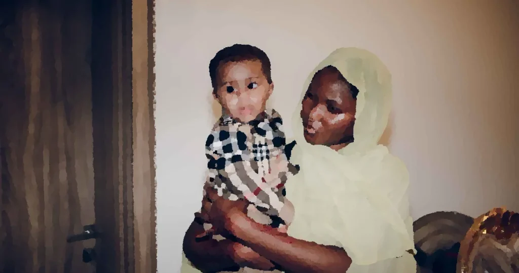 A mother lovingly holds her baby while indoors, showcasing their cultural attire.
