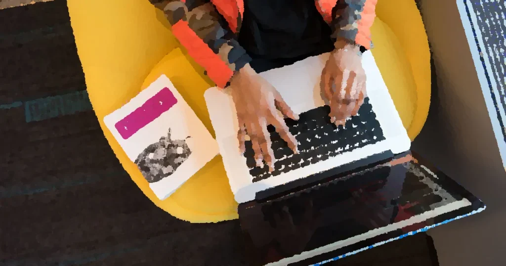 A developer typing code on a laptop with a Python book beside in an office.