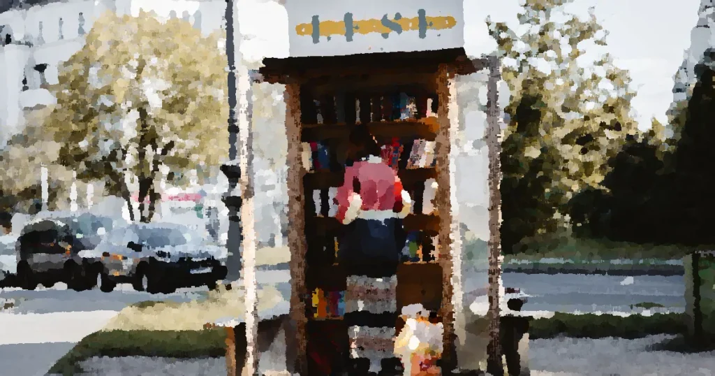 Person using a free library stand on a sunny day with cars and buildings nearby.