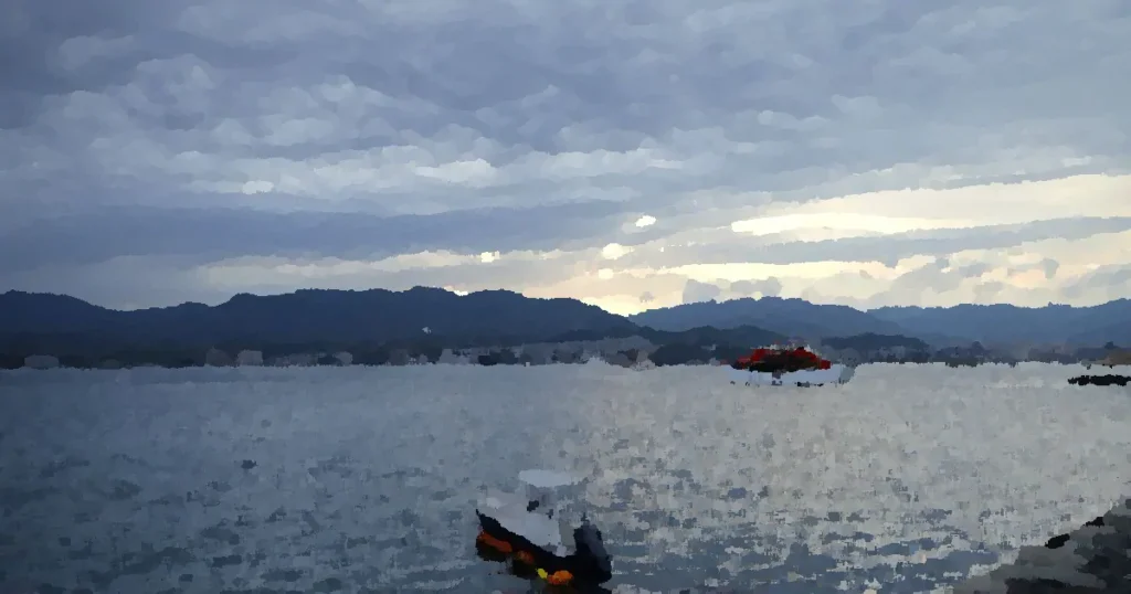 A serene view of Hiroshima's coastline with boats and mountains under a cloudy sky.