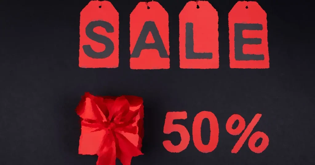 Red gift box next to sale tags and 50% sign on black background, ideal for promotions.