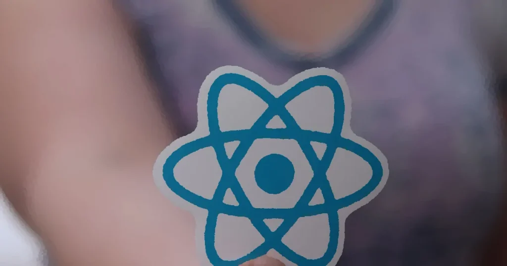 A person holds a sticker featuring the React logo, commonly used in web development.